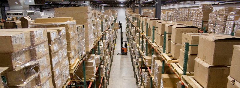 Third party logistic shipping warehouse filled with boxes on shelves and man standing next to a forklift