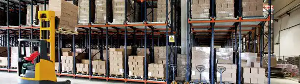 logistics warehouse with boxes stacked on shelves and man driving a forklift